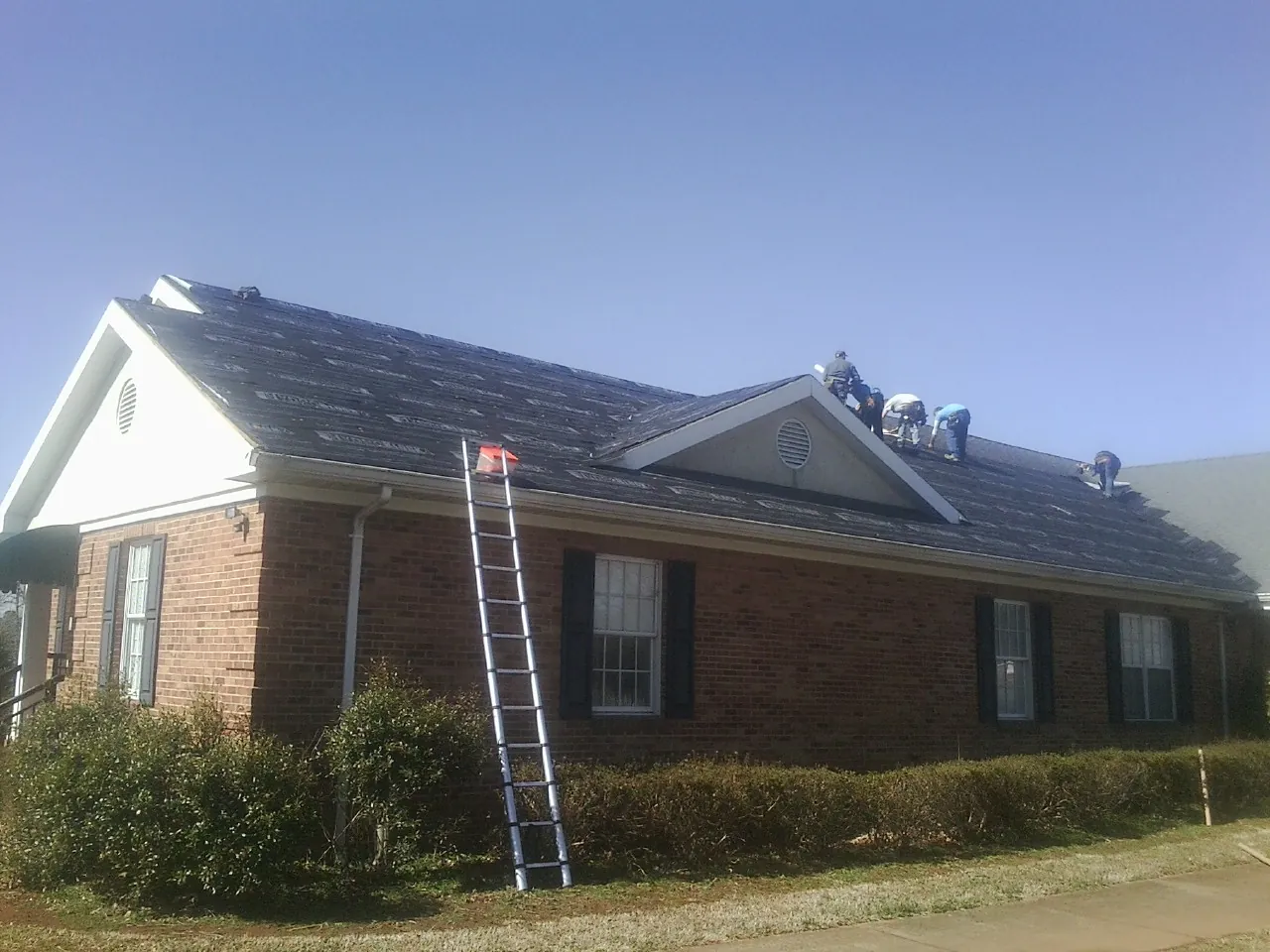 Crew tearing shingles off a brick ranch roof with a ladder set — Metal Roof Repair work by our crew in Lake Stevens