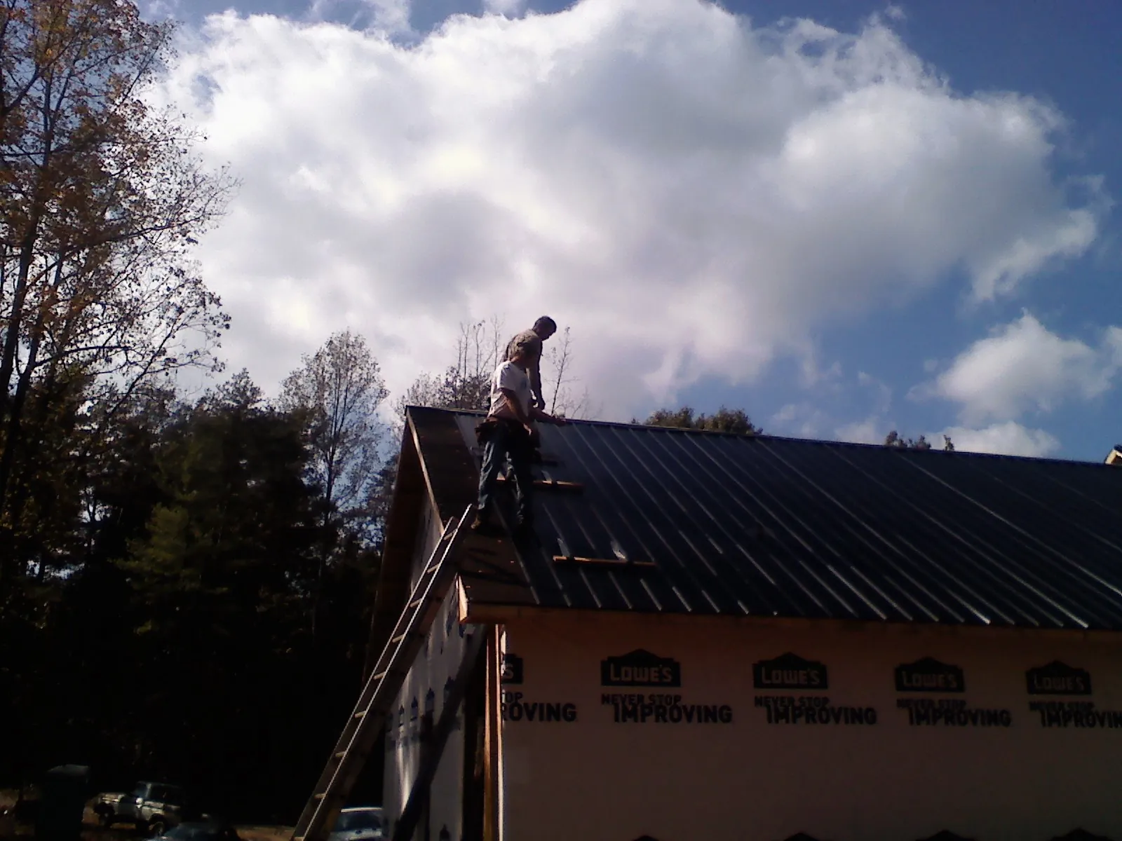 Roofer fastening dark metal panels high against a cloudy sky, from a Roof Inspection job in Lake Stevens
